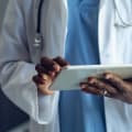 Healthcare clinical professional in white coat and a stethoscope uses a tablet computer.